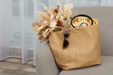 Photo of Stylish beach bag with beautiful bouquet of dried flowers, sunglasses and magazine on sofa in room