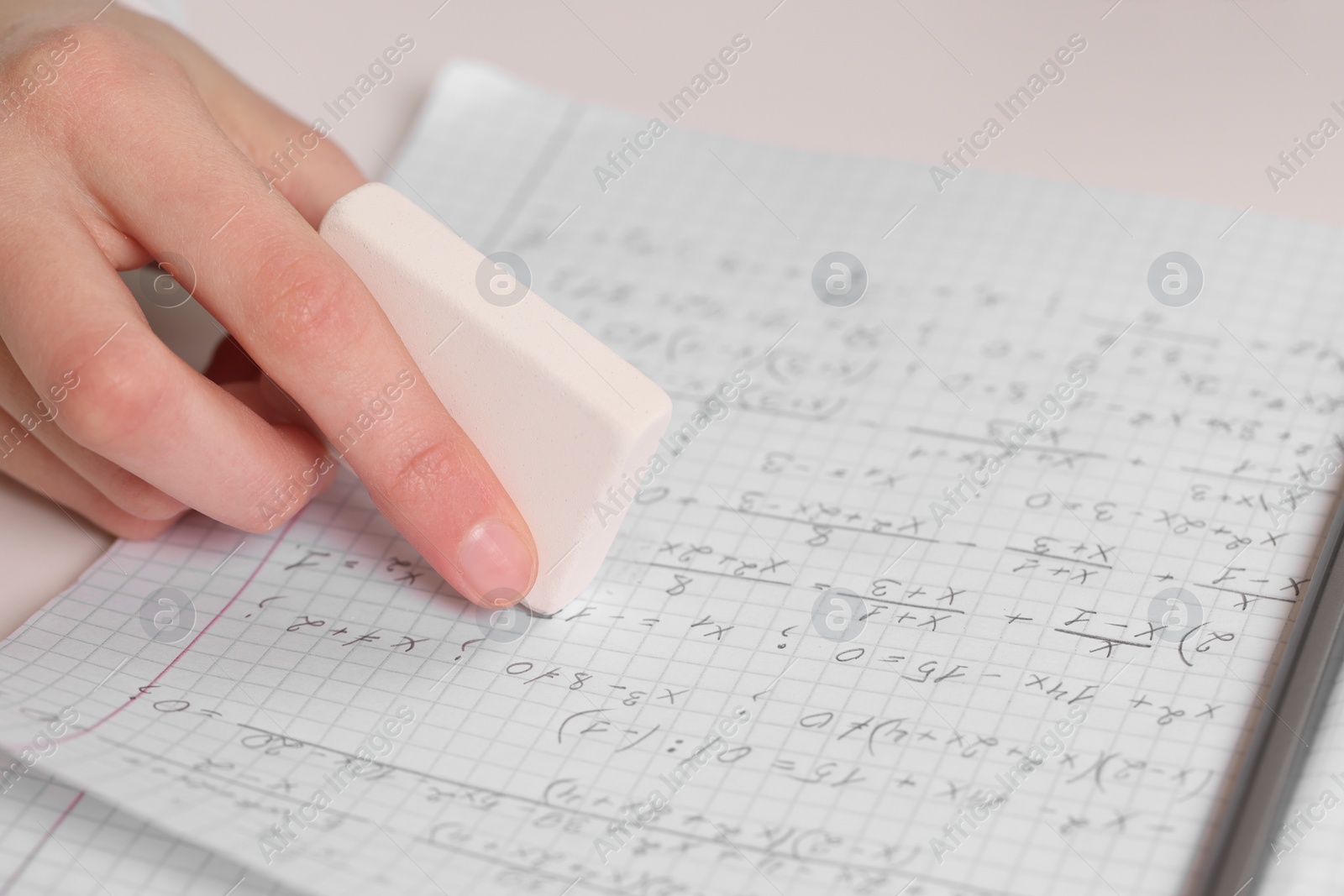 Photo of Girl erasing mistake in her notebook at white desk, closeup