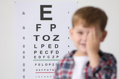 Photo of Little boy covering her eye against vision test chart, selective focus