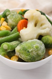 Photo of Mix of different frozen vegetables in bowl on white wooden table, closeup