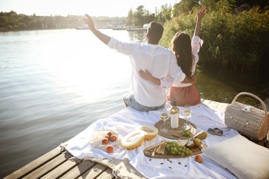 Photo of Happy couple spending time on pier at picnic, back view