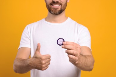 Photo of Man with condom showing thumb up on yellow background, closeup. Safe sex
