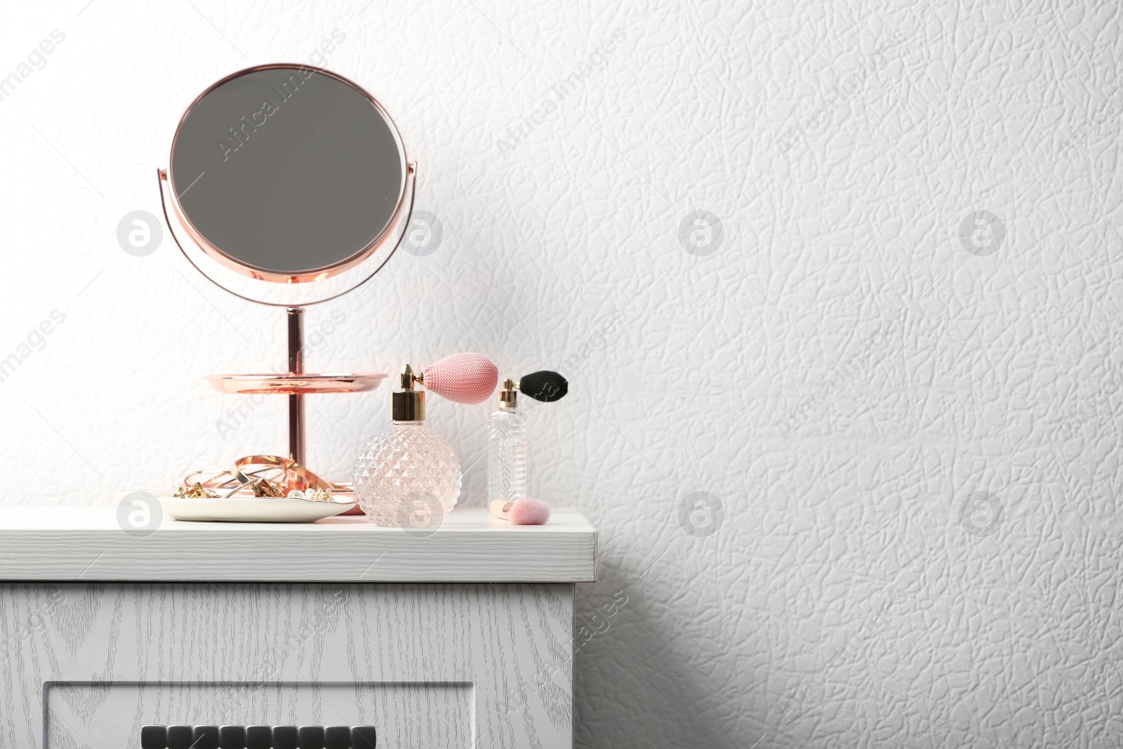 Photo of Perfume bottles and jewellery on dressing table. Space for text