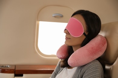 Photo of Young woman with travel pillow and mask sleeping in airplane during flight