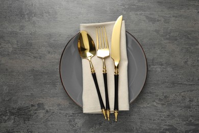 Photo of Elegant setting with golden cutlery on dark grey table, top view