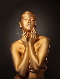 Photo of Portrait of beautiful lady with gold paint on skin against black background