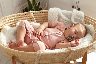 Photo of Cute little baby with pacifier sleeping in wicker crib at home