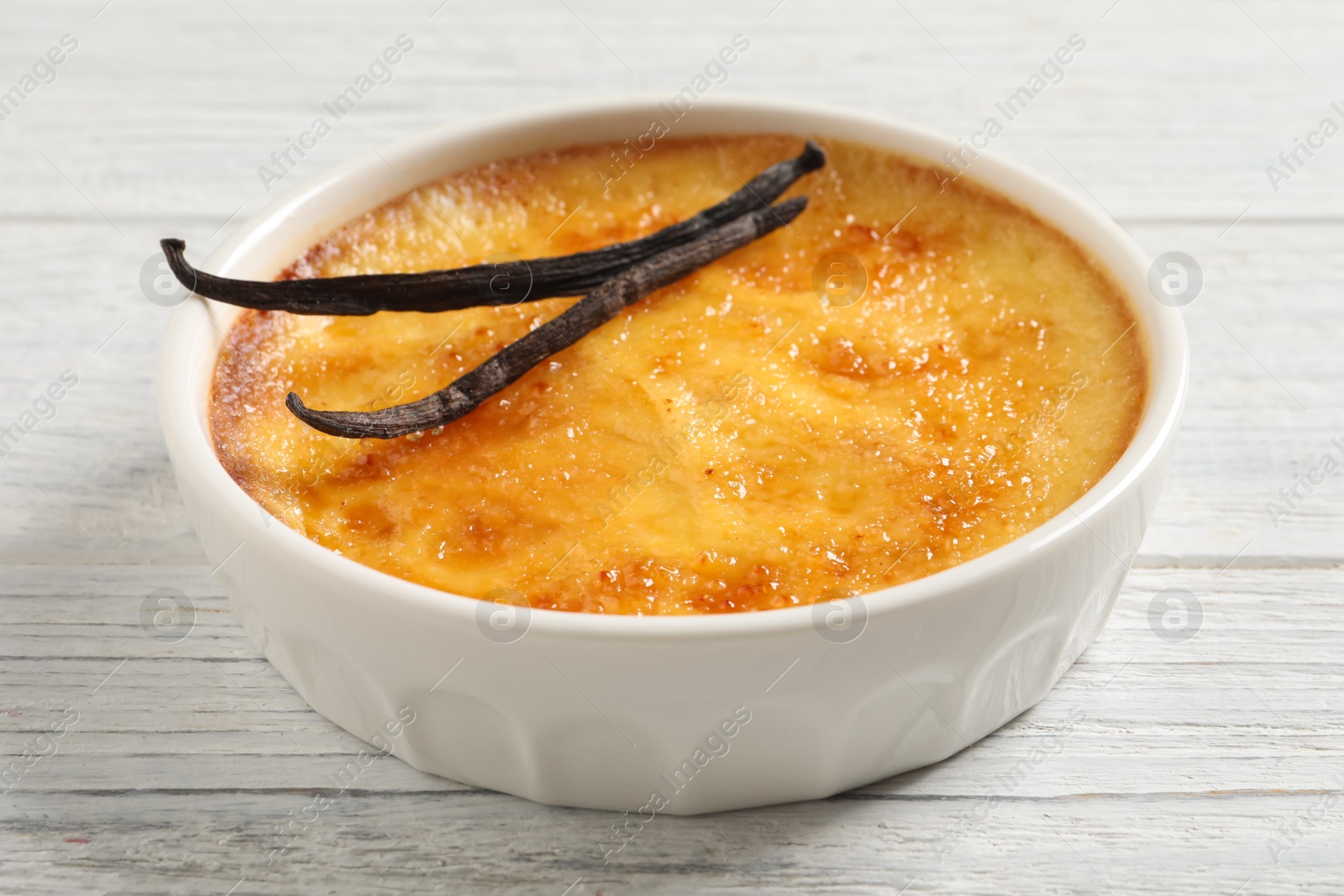 Photo of Delicious creme brulee and vanilla sticks on white wooden table, closeup view