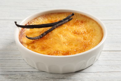 Delicious creme brulee and vanilla sticks on white wooden table, closeup view