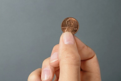 Photo of Young woman holding coin on grey background, closeup view