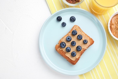 Photo of Flat lay composition of toast with peanut butter and blueberries on white table. Healthy breakfast
