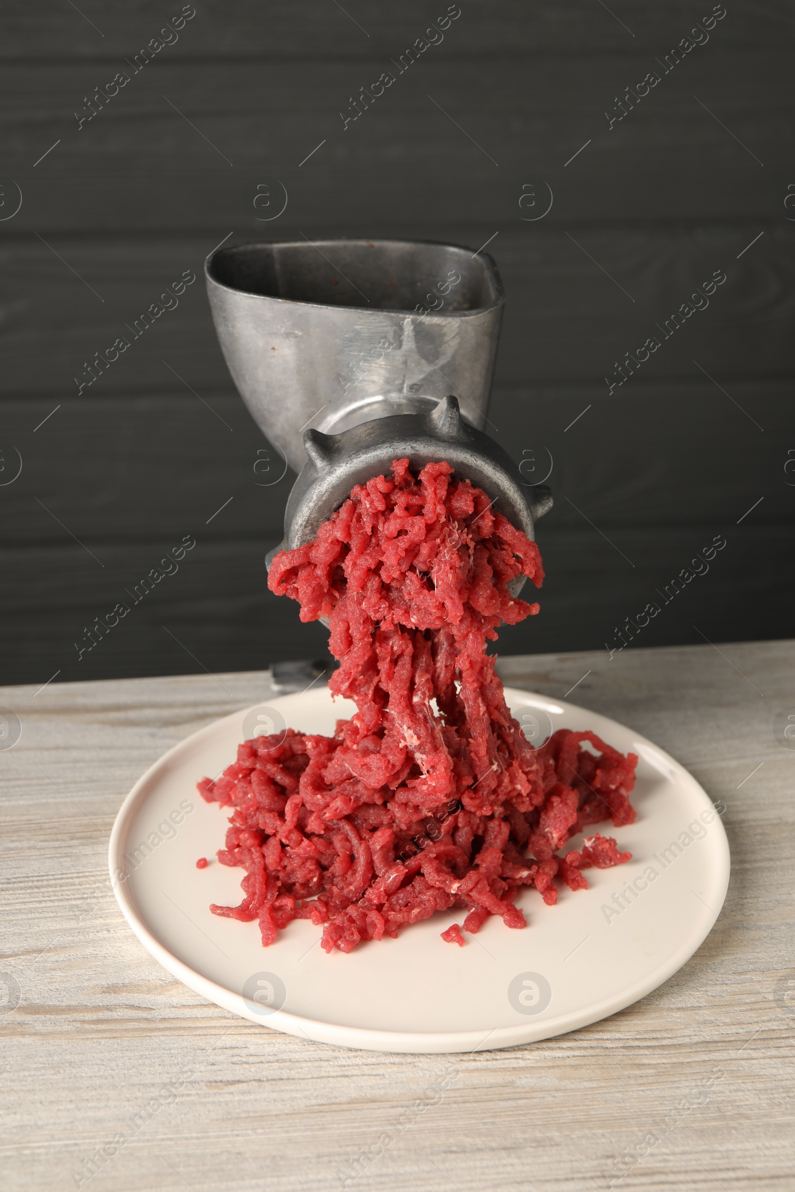 Photo of Metal meat grinder with beef mince on light wooden table