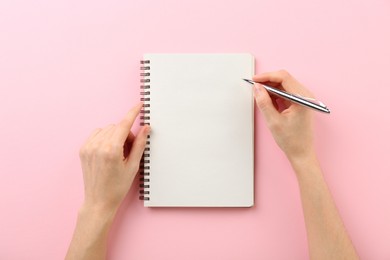 Photo of Woman writing in notebook on pink background, top view