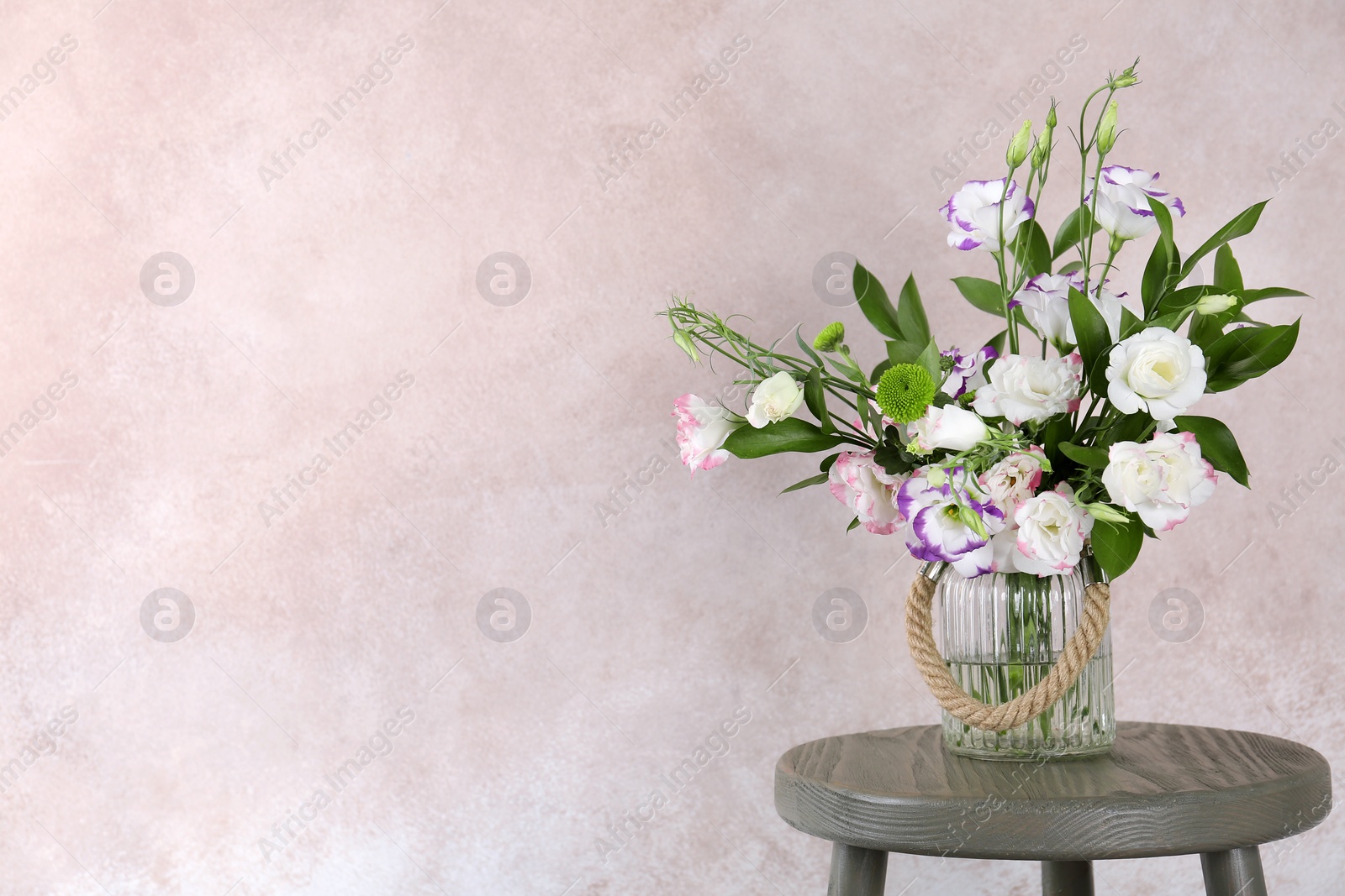 Photo of Vase with bouquet of beautiful flowers on table against color background. Space for text