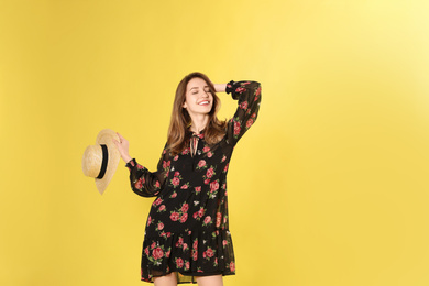 Photo of Young woman wearing floral print dress with straw hat on yellow background