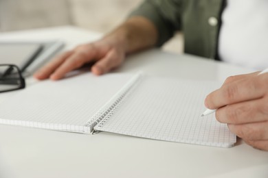 Photo of Left-handed man writing in notebook at white table, closeup