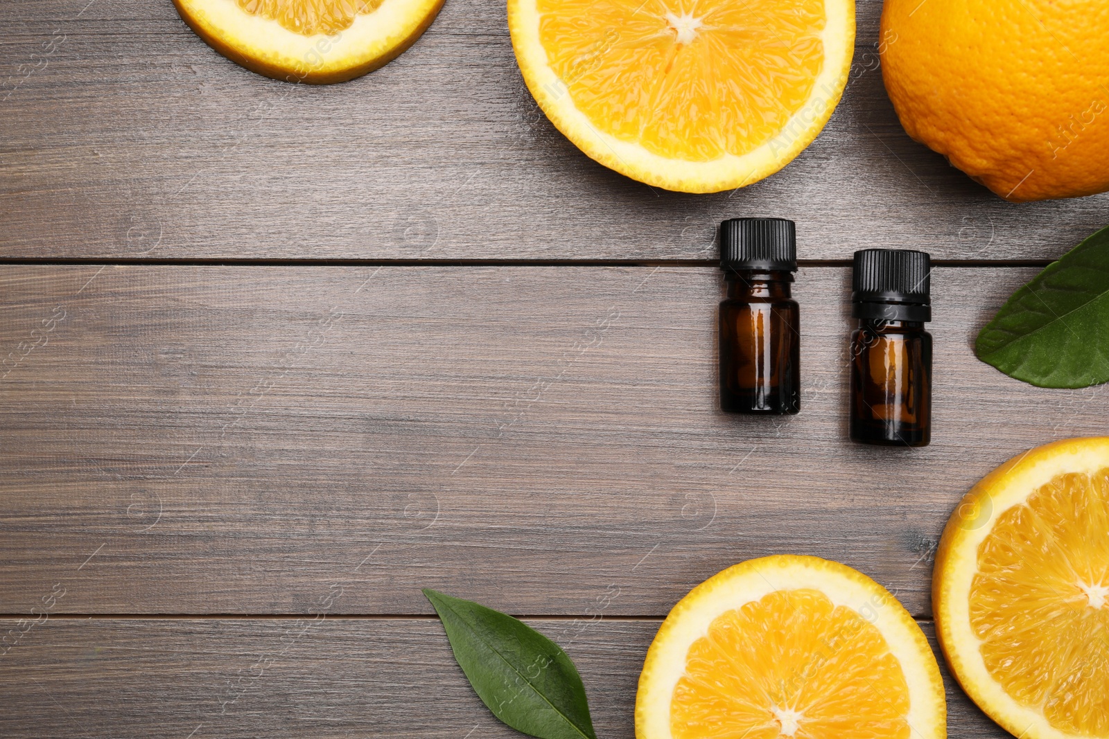 Photo of Bottles of essential oil with orange slices and leaves on wooden table, flat lay. Space for text