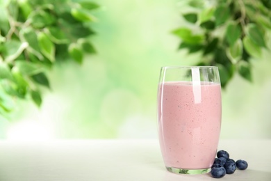 Photo of Tasty fresh milk shake and blueberries on white table. Space for text