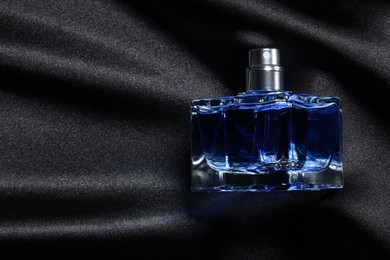 Photo of Luxury men's perfume in bottle on black satin fabric, top view. Space for text