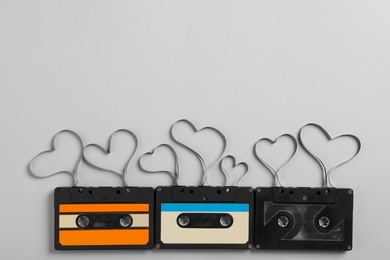 Photo of Music cassettes and hearts made of tape on light grey background, flat lay with space for text. Listening love songs