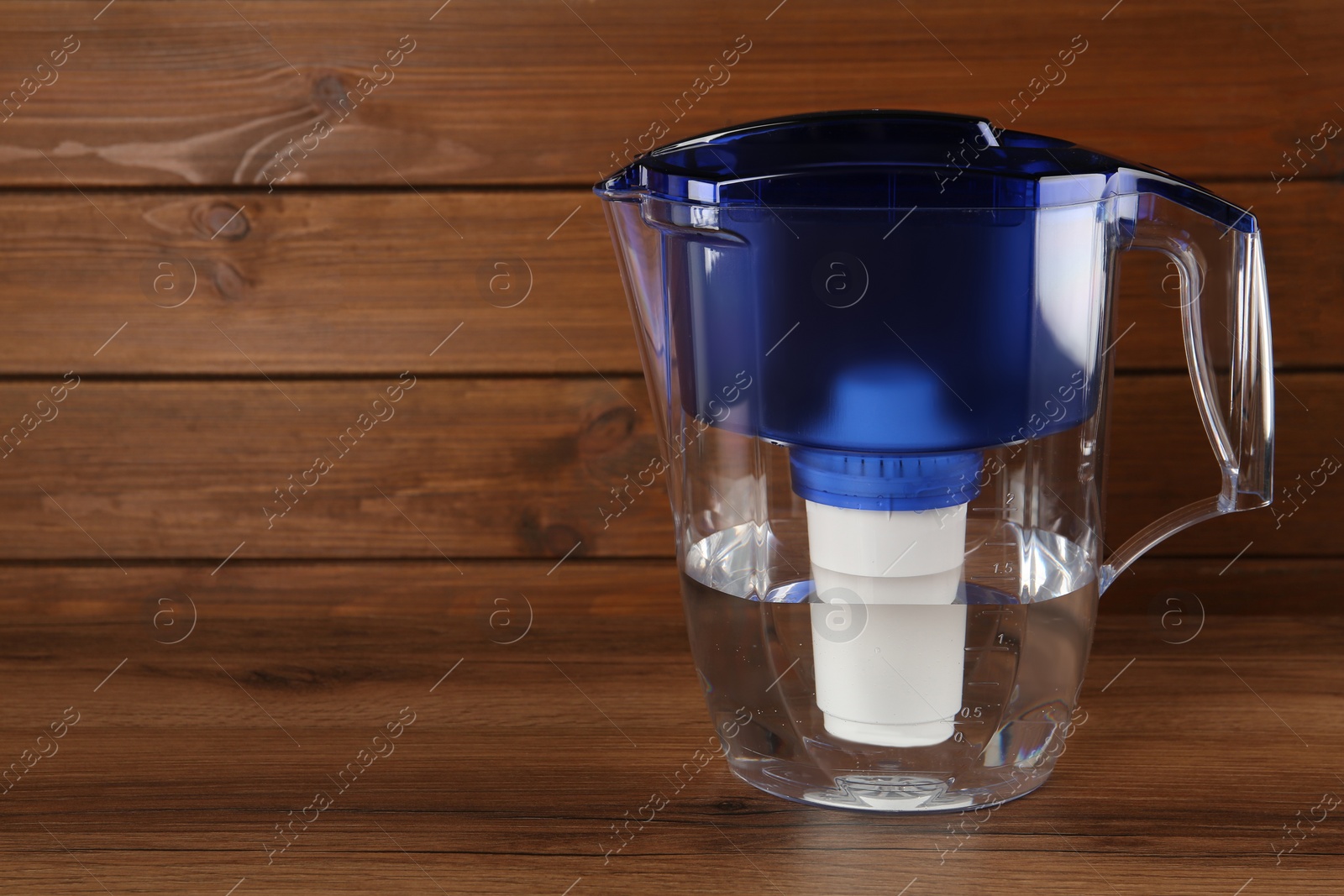 Photo of Filter jug with purified water on wooden table. Space for text