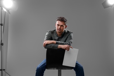 Photo of Casting call. Man with script sitting on chair against grey background in studio