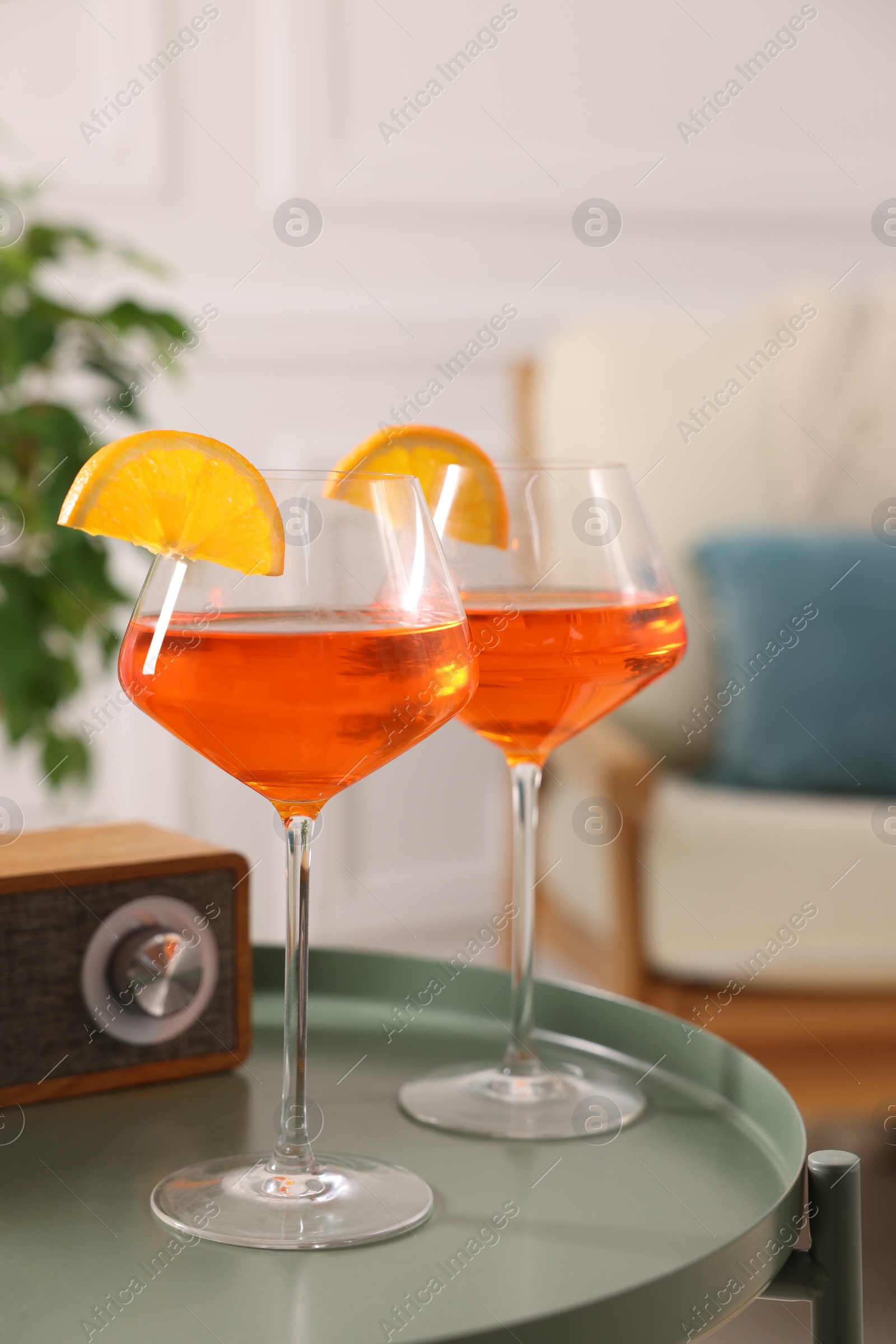 Photo of Tasty cocktail in glasses with orange slices and radio set on table in room. Relax at home