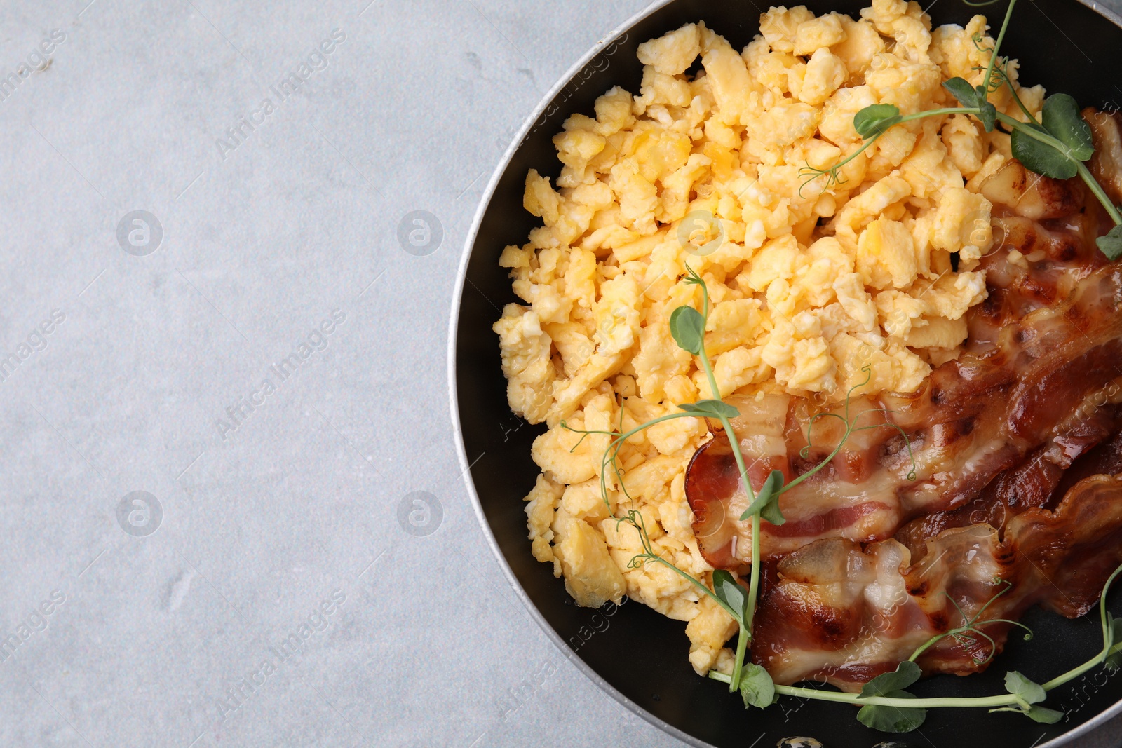 Photo of Delicious scrambled eggs with bacon in frying pan on grey table, top view. Space for text