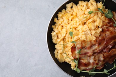 Photo of Delicious scrambled eggs with bacon in frying pan on grey table, top view. Space for text