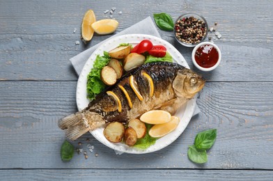 Photo of Tasty homemade roasted crucian carp served on grey wooden table, flat lay. River fish