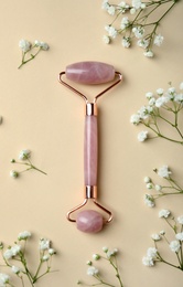 Photo of Natural face roller and flowers on beige background, flat lay