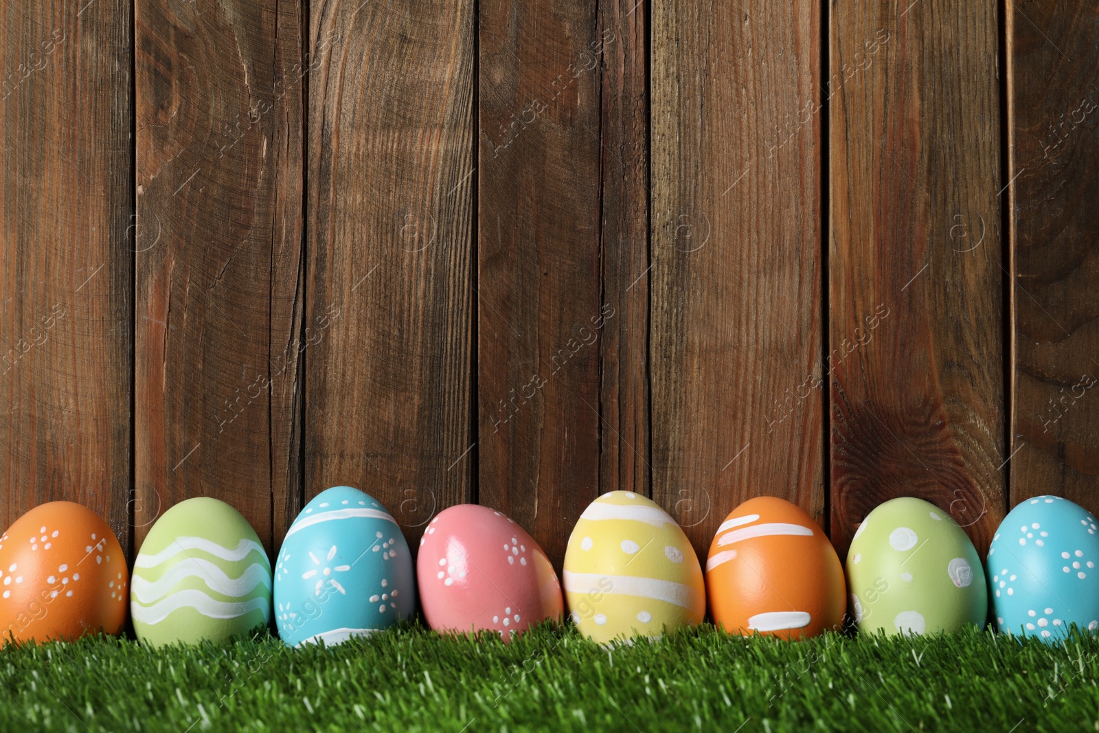 Photo of Colorful painted Easter eggs on green grass against wooden background, space for text