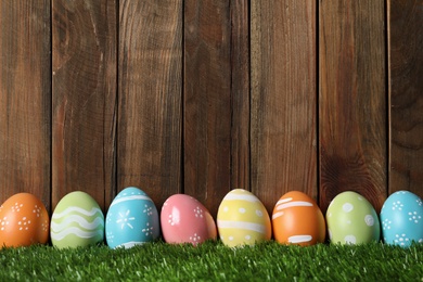 Photo of Colorful painted Easter eggs on green grass against wooden background, space for text