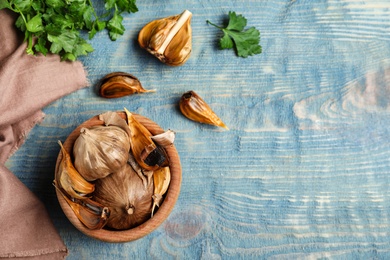 Photo of Flat lay composition with bowl of black garlic on blue wooden table. Space for text