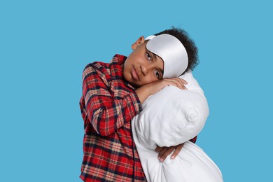 Boy with pillow and sleep mask on light blue background. Insomnia problem