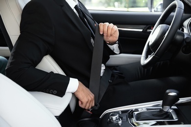 Photo of Driver fastening safety belt in luxury car, focus on hands