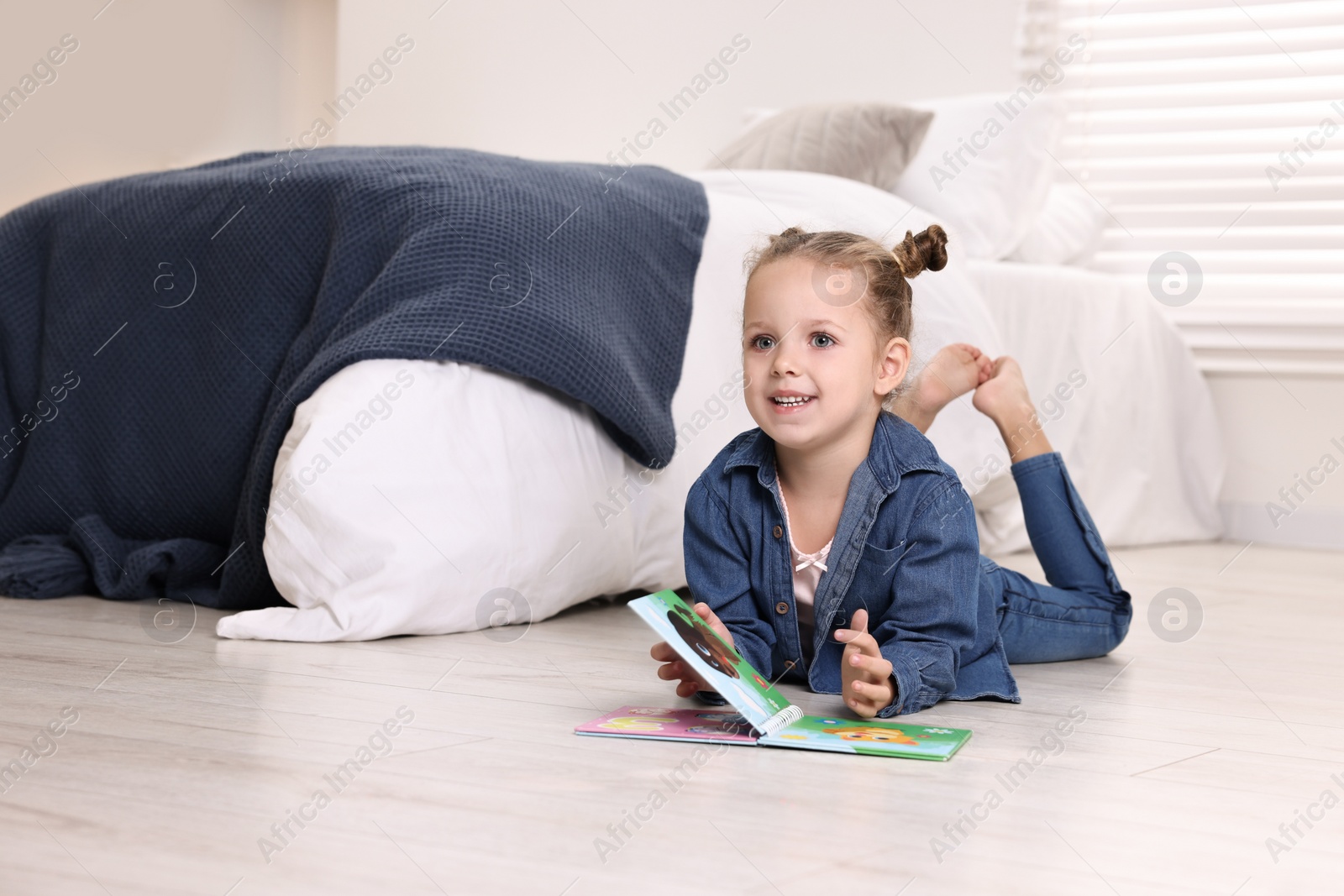 Photo of Cute little girl with book on warm floor at home, space for text. Heating system