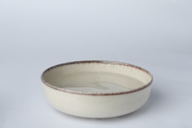 Beige bowl full of water on white background