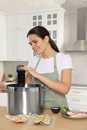 Photo of Woman using thermal immersion circulator at table in kitchen. Sous vide cooking