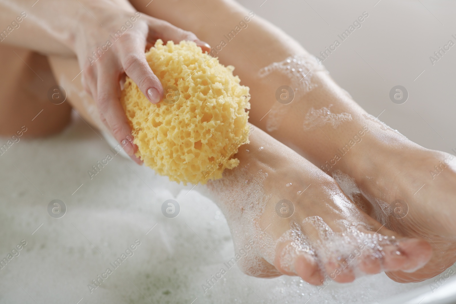 Photo of Woman rubbing her leg with sponge while taking bath, closeup