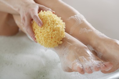 Photo of Woman rubbing her leg with sponge while taking bath, closeup