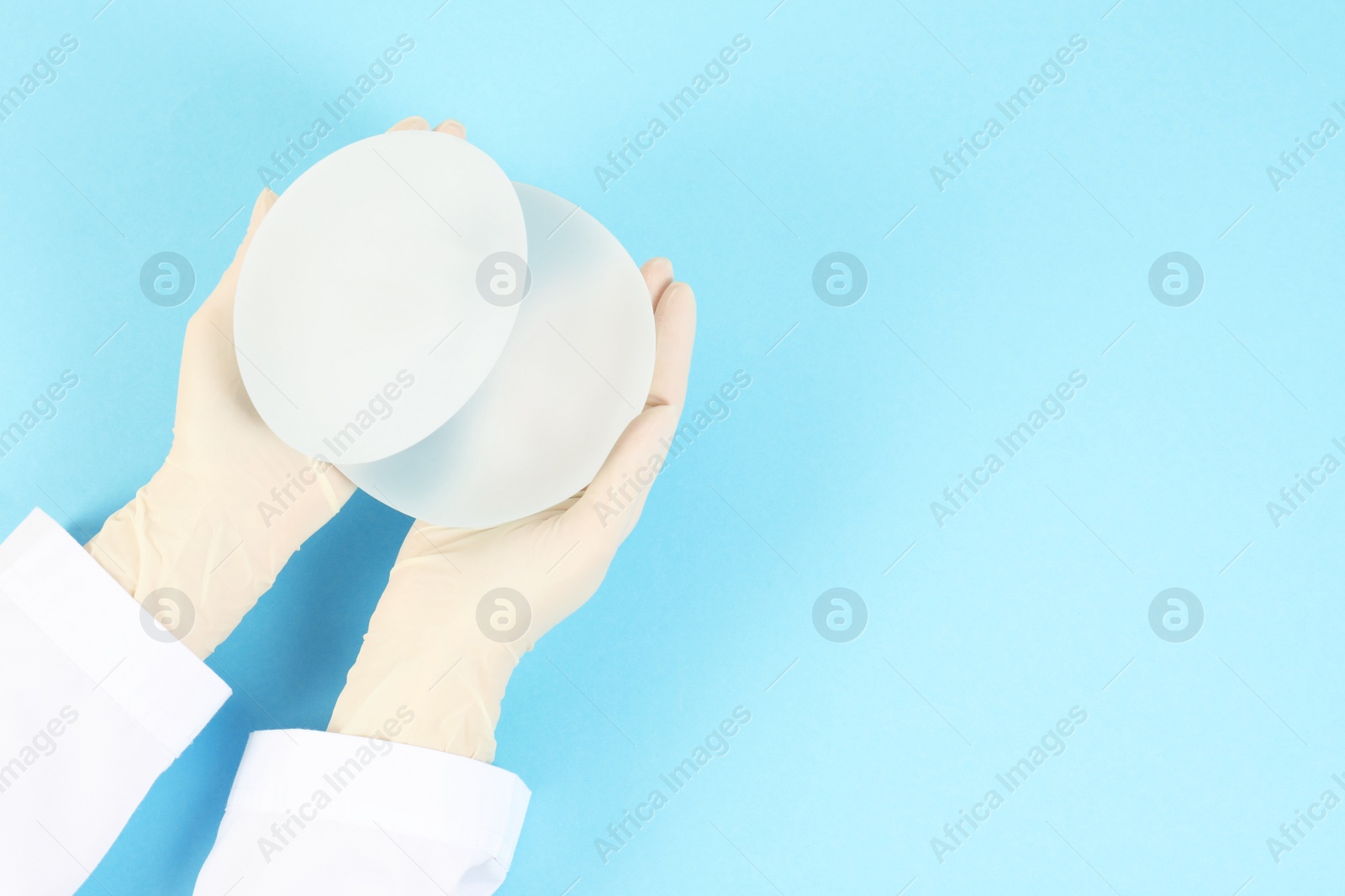 Photo of Doctor holding silicone implants for breast augmentation on color background, top view with space for text. Cosmetic surgery