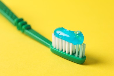 Photo of Green brush with toothpaste on yellow background, closeup