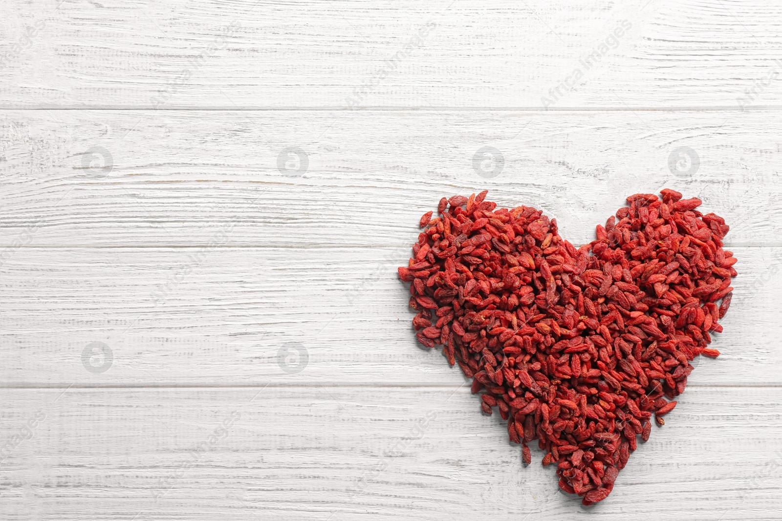 Photo of Heart made of dried goji berries on white wooden table, top view with space for text. Healthy superfood