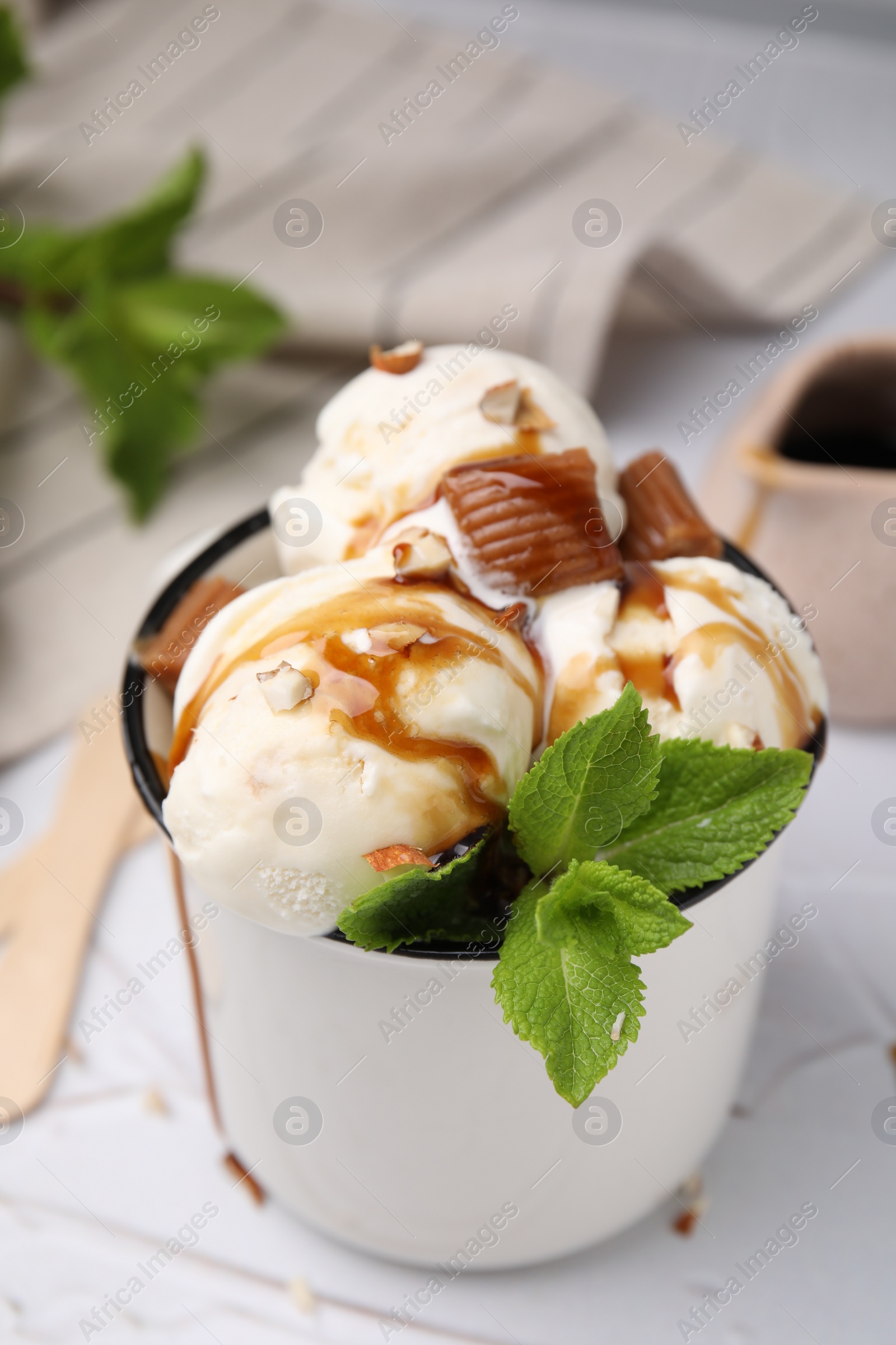 Photo of Scoops of ice cream with caramel sauce, candies and mint leaves on white textured table, closeup