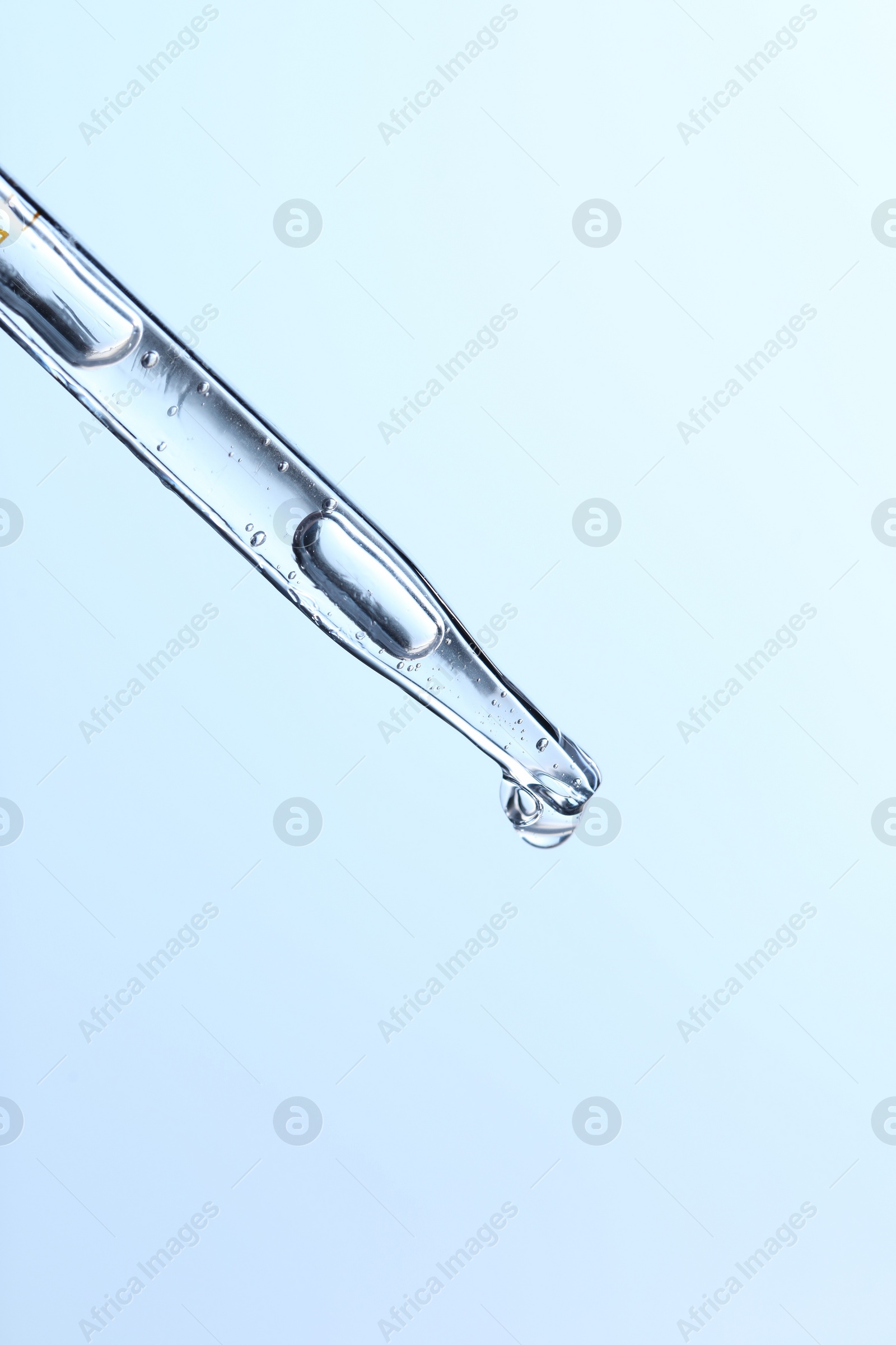 Photo of Dripping liquid from pipette on light blue background, closeup