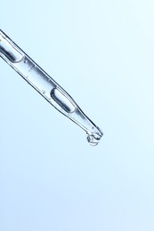 Dripping liquid from pipette on light blue background, closeup