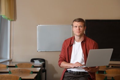 Portrait of male teacher with laptop in modern classroom