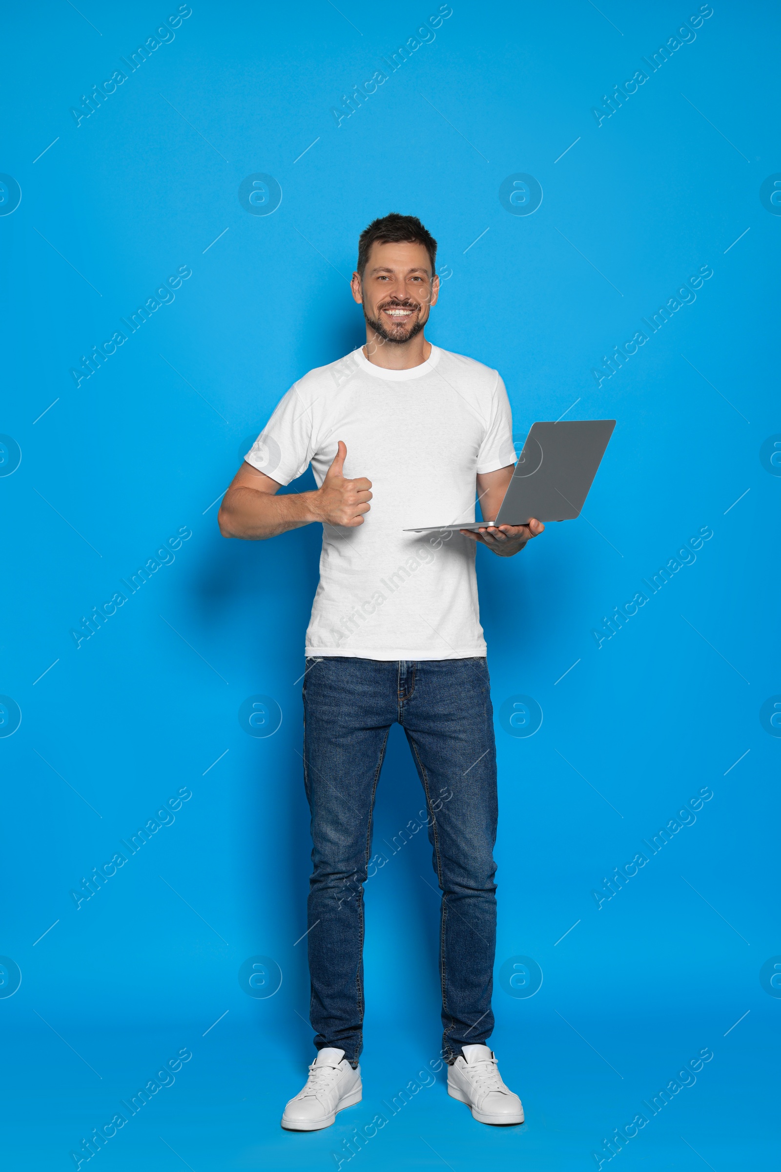 Photo of Handsome man with laptop showing thumbs up on light blue background