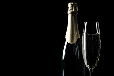 Bottle and glass of champagne on black background, space for text